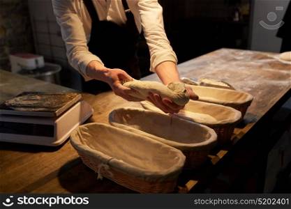 food cooking, baking and people concept - chef or baker putting yeast bread dough into baskets for rising at bakery kitchen. baker with dough rising in baskets at bakery