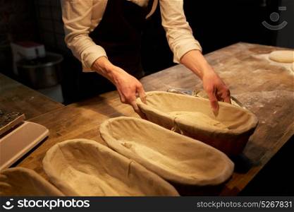 food cooking, baking and people concept - chef or baker putting yeast bread dough into baskets for rising at bakery kitchen. baker with dough rising in baskets at bakery