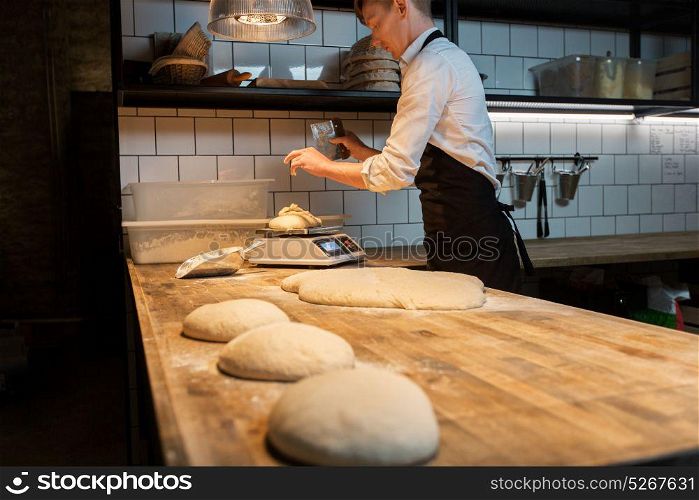 food cooking, baking and people concept - chef or baker with bench cutter portioning and weighing dough on scale at bakery kitchen. chef or baker weighing dough on scale at bakery