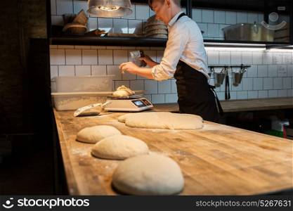 food cooking, baking and people concept - chef or baker with bench cutter portioning and weighing dough on scale at bakery kitchen. chef or baker weighing dough on scale at bakery
