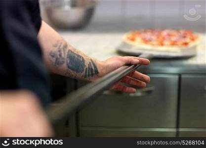 food cooking, culinary and people concept - cook or baker hand with pizza on peel at pizzeria. cook or baker hand with pizza on peel at pizzeria