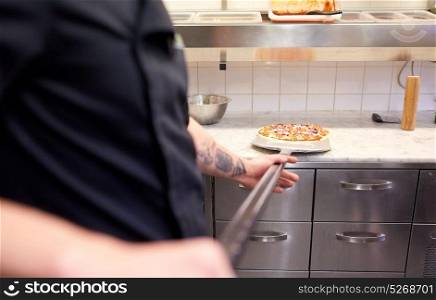 food cooking, culinary and people concept - cook or baker hands with pizza on peel at pizzeria. cook or baker with pizza on peel at pizzeria