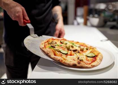 food cooking, culinary and people concept - cook or baker placing pizza from peel to plate at pizzeria. cook with baked pizza on peel at pizzeria