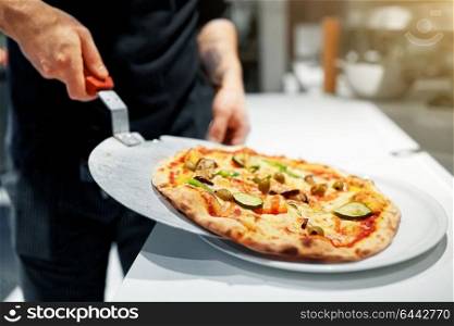 food cooking, culinary and people concept - cook or baker placing pizza from peel to plate at pizzeria. cook with baked pizza on peel at pizzeria