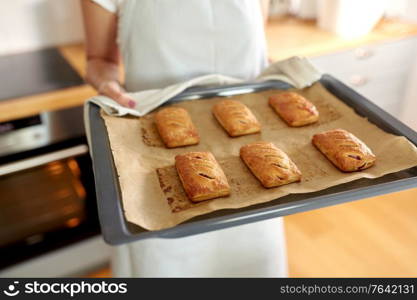 food cooking, culinary and people concept - young woman with towel holding hot baking tray with jam pies at home kitchen. woman holding baking tray with pies at kitchen
