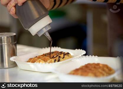 food, cooking, dessert and people concept - close up of cook adding chocolate syrop to waffle. close up of cook adding syrop to waffle
