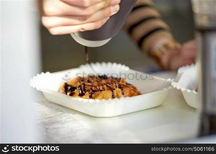 food, cooking, dessert and people concept - close up of cook adding chocolate syrup to waffle. close up of cook adding syrup to waffle