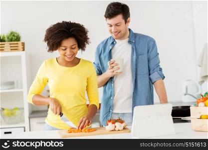 food, cooking, people, international and healthy eating concept - happy couple with tablet pc computer chopping vegetables and talking at home kitchen. happy couple cooking food at home kitchen