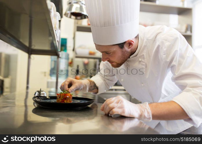 food cooking, profession and people concept - happy male chef cook serving and garnishing stewed vegetables on plate at restaurant kitchen. happy male chef cooking food at restaurant kitchen