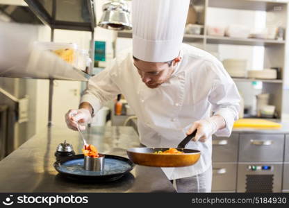 food cooking, profession and people concept - happy male chef cook with frying pan and spoon serving stewed vegetables on plate at restaurant kitchen. happy male chef cooking food at restaurant kitchen