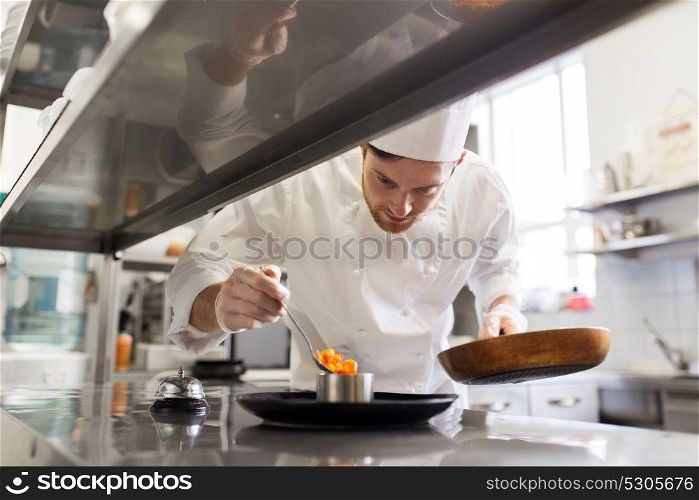 food cooking, profession and people concept - happy male chef cook with frying pan and spoon serving stewed vegetables on plate at restaurant kitchen. happy male chef cooking food at restaurant kitchen