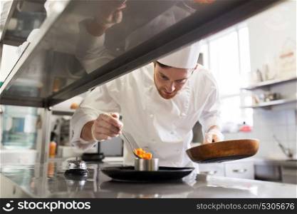 food cooking, profession and people concept - happy male chef cook with frying pan and spoon serving stewed vegetables on plate at restaurant kitchen. happy male chef cooking food at restaurant kitchen