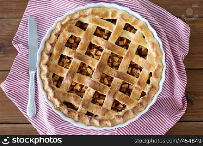 food, culinary and baking concept - close up of apple pie in baking mold with knife on kitchen towel. close up of apple pie in baking mold and knife