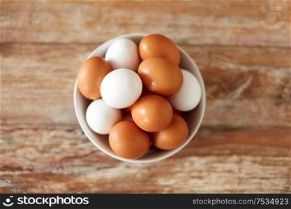 food, culinary and cooking concept - close up of natural chicken eggs in ceramic bowl on wooden table. close up of eggs in ceramic bowl on wooden table
