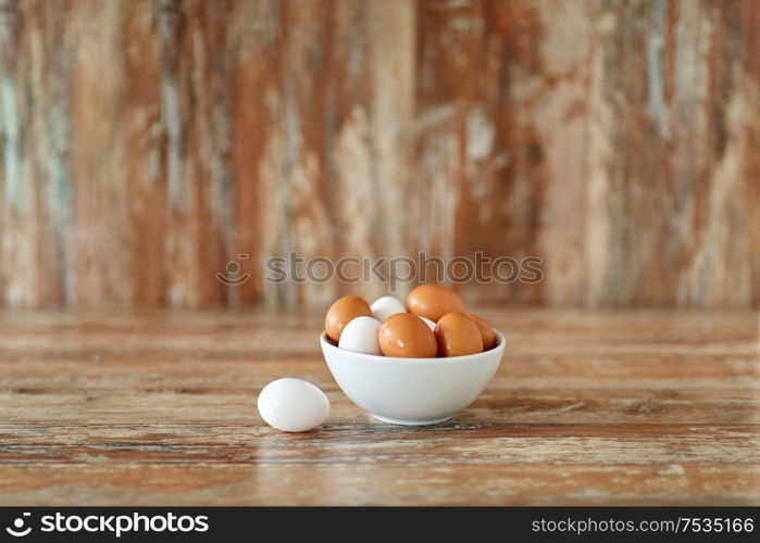 food, culinary and cooking concept - close up of natural chicken eggs in ceramic bowl on wooden table. close up of eggs in ceramic bowl on wooden table