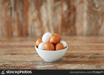 food, culinary and cooking concept - close up of natural chicken eggs in ceramic bowl on wooden table. close up of eggs in ceramic bowl on wooden table