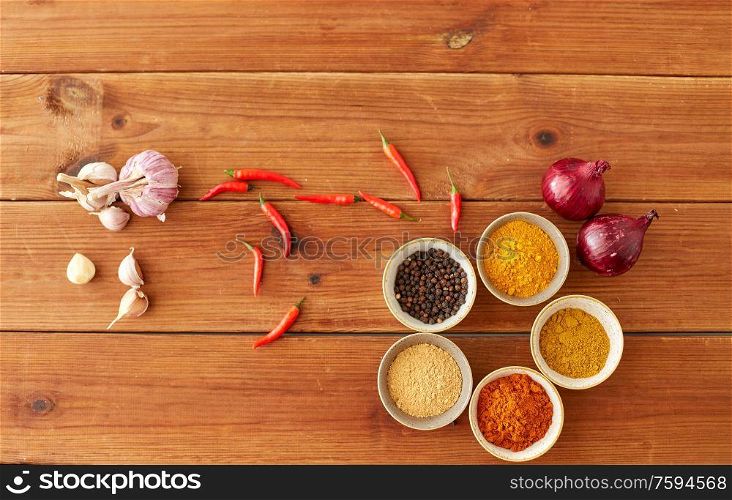 food, culinary and eating concept - bowls with different spices, onion, garlic and red hot chili peppers on wooden table. spices, onion, garlic and red hot chili peppers