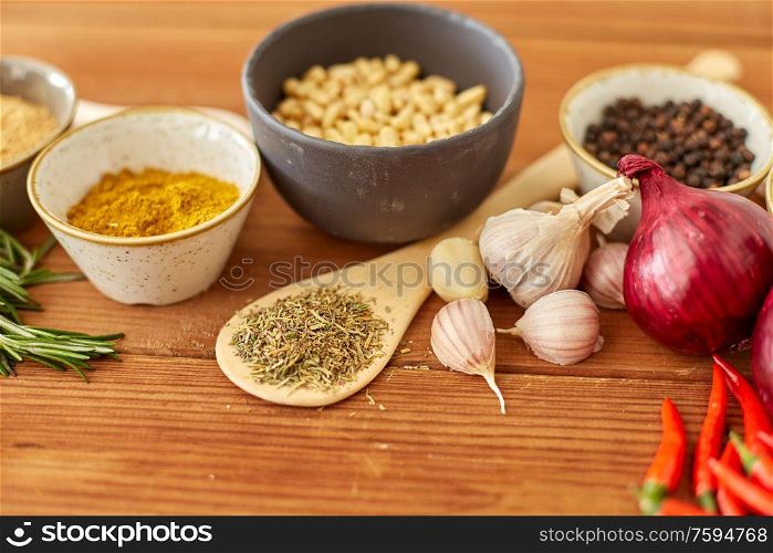 food, culinary and eating concept - bowls with different spices, onion, garlic with pine nuts and red hot chili pepper on wooden table. spices, onion, garlic, pine nuts and chili peppers