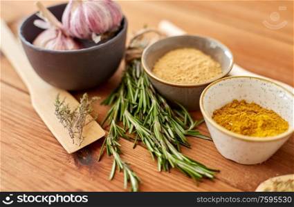 food, culinary and eating concept - bowls with different spices, rosemary, spatula and garlic on wooden table. spices, rosemary, wooden spatula and garlic