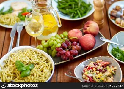 food, culinary and eating concept - fruits, salads, jug of orange water and pasta on wooden table. fruits, salads and pasta on wooden table
