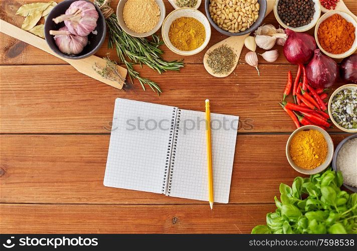 food, culinary and eating concept - notebook with pencil among different spices, onion, garlic with pine nuts and red hot chili peppers on wooden table. notebook with pencil among spices on wooden table