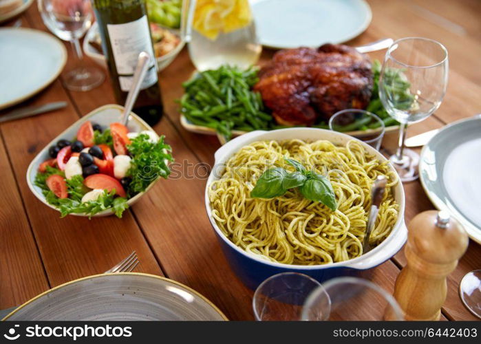 food, culinary and eating concept - pasta with basil in bowl and other food on wooden table. pasta with basil in bowl and other food on table