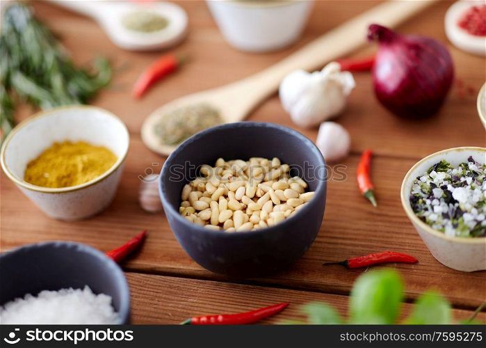 food, culinary and eating concept - pine nuts in bowl and spices on wooden kitchen table. pine nuts in bowl and spices on kitchen table
