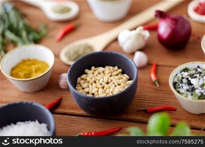 food, culinary and eating concept - pine nuts in bowl and spices on wooden kitchen table. pine nuts in bowl and spices on kitchen table
