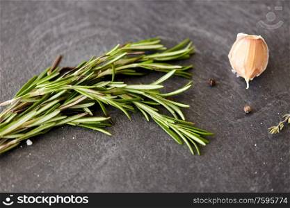 food, culinary and eating concept - rosemary, garlic and black pepper on stone surface. rosemary, garlic and black pepper on stone surface