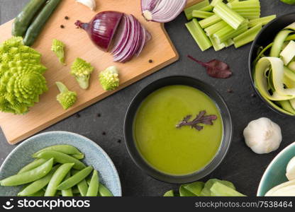 food, culinary and healthy eating concept - close up of different green vegetables and cream soup in ceramic bowl on slate stone background. green vegetables and cream soup in ceramic bowl