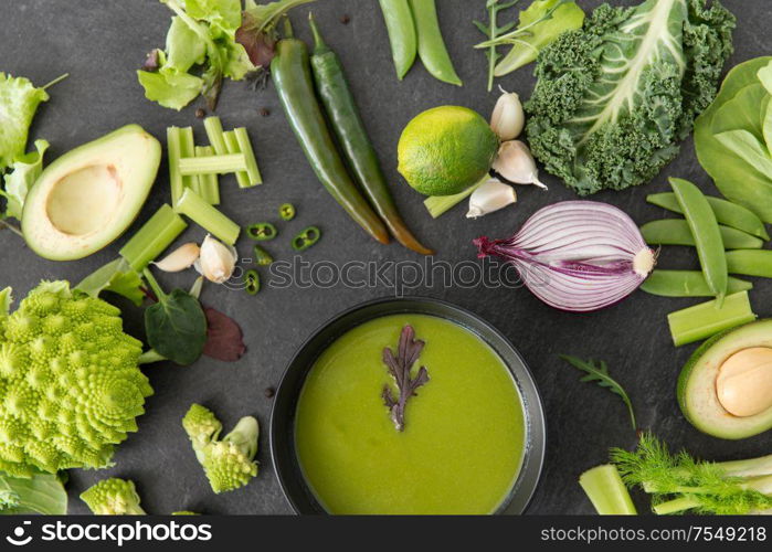 food, culinary and healthy eating concept - close up of different green vegetables and cream soup in ceramic bowl on slate stone background. green vegetables and cream soup in ceramic bowl