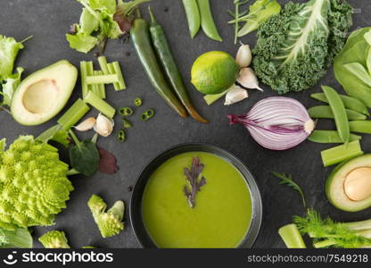 food, culinary and healthy eating concept - close up of different green vegetables and cream soup in ceramic bowl on slate stone background. green vegetables and cream soup in ceramic bowl