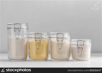 food, culinary and storage concept - jars with different kinds of flour on white background. close up of jars with different flours on table