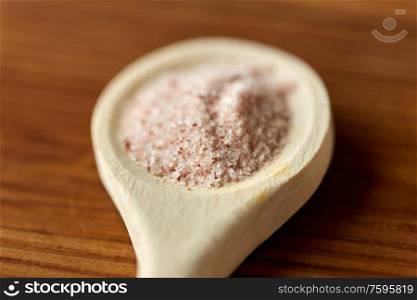 food, culinary and unhealthy eating concept - close up of wooden spoon with pink himalayan salt. close up of wooden spoon with pink himalayan salt