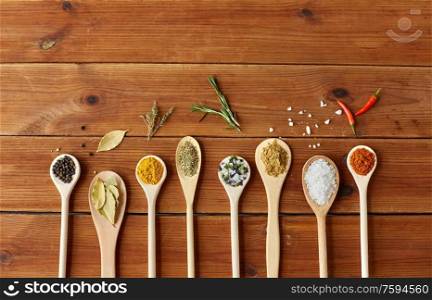 food, culinary and unhealthy eating concept - spoons with different spices and salt on wooden table. spoons with spices and salt on wooden table