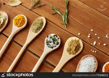 food, culinary and unhealthy eating concept - spoons with different spices and salt on wooden table. spoons with spices and salt on wooden table