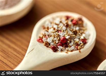 food, culinary and unhealthy eating concept - spoons with salt and pink peppercorn spice on wooden table. spoon with salt and spices on wooden table
