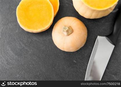 food, culinary and vegetable concept - cut pumpkin and kitchen knife on stone background. cut pumpkin and kitchen knife on stone background