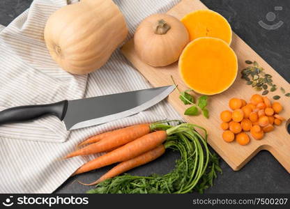 food, culinary and vegetable concept - cut pumpkin, carrots, linen towel and kitchen knife on table. cut pumpkin, carrots and kitchen knife on table