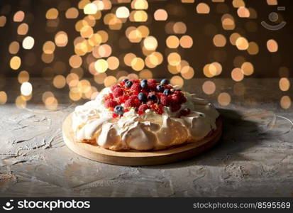 food, culinary, baking and cooking concept - close up of pavlova meringue cake decorated with berries on wooden serving board over dark background with filghts. pavlova meringue cake with berries on wooden board