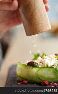 food, culinary, eating and people concept - close up of hand with salt shaker seasoning brie cheese salad at restaurant or cafe