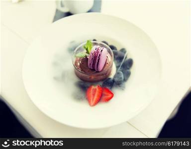 food, culinary, haute cuisine and cooking concept - close up of chocolate dessert with macaron cookie and fresh strawberry at restaurant