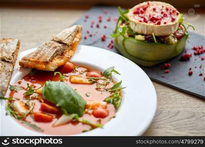 food, culinary, haute cuisine and cooking concept - goat cheese salad with vegetables and dried raspberries and plate of gazpacho soup at restaurant or cafe