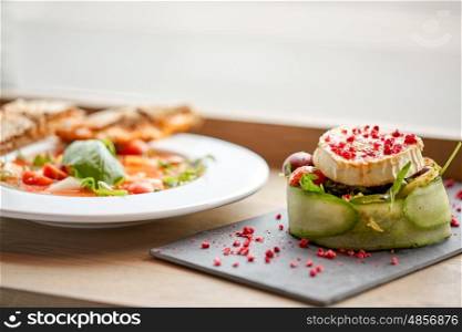 food, culinary, haute cuisine and cooking concept - goat cheese salad with vegetables and dried raspberries and plate of gazpacho soup at restaurant or cafe
