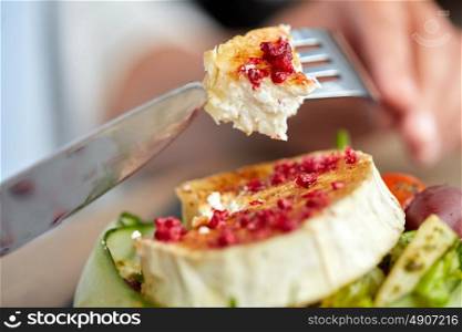 food, culinary, haute cuisine and people concept - close up of woman eating goat cheese salad with vegetables and dried raspberries using fork and knife at restaurant or cafe. close up of woman eating goat cheese salad