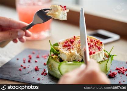 food, culinary, haute cuisine and people concept - woman eating goat cheese salad with fork and knife at restaurant or cafe