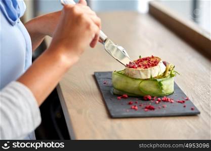 food, culinary, haute cuisine and people concept - woman eating goat cheese salad with vegetables and dried raspberries using fork and knife at restaurant or cafe. woman eating goat cheese salad at restaurant