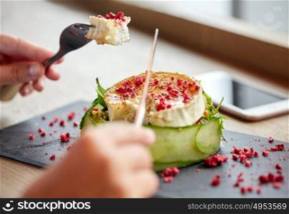 food, culinary, haute cuisine and people concept - woman eating goat cheese salad with fork and knife at restaurant or cafe. woman eating goat cheese salad at restaurant