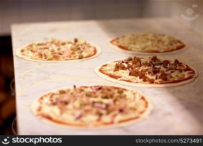 food, culinary, italian cuisine and cooking concept - raw pizza with grated cheese on table at pizzeria. raw pizza with grated cheese on table at pizzeria