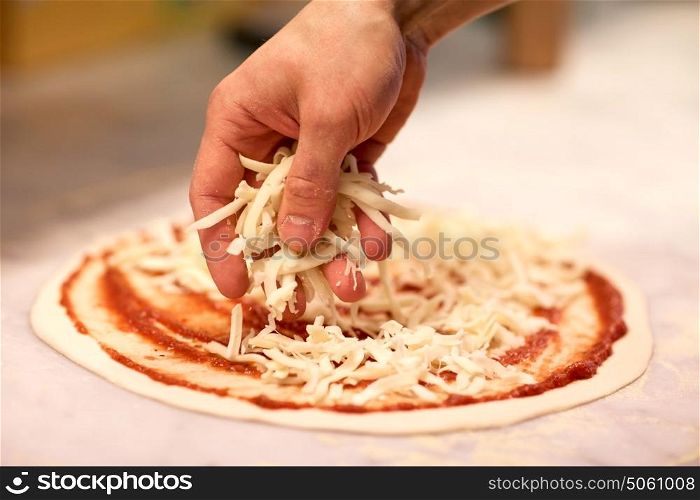 food, culinary, italian cuisine, people and cooking concept - cook hand adding grated cheese to pizza at pizzeria. cook hand pouring cheese to pizza at pizzeria
